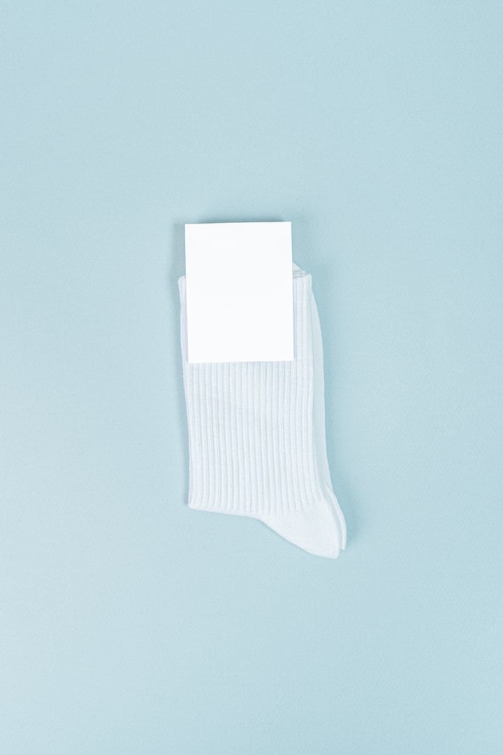White ribbed crew sock with a blank branding card tucked into the cuff, on a light blue backdrop